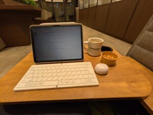 空港のラウンジでiPadとキーボードを広げ、コーヒーを飲みながら文章を書いている様子